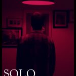 Poster for Solo, a film about love. A person is viewed from behind staring at a framed picture under red light.