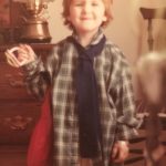 Photo of a child smiling and wearing an oversized shirt, scarf and purse.